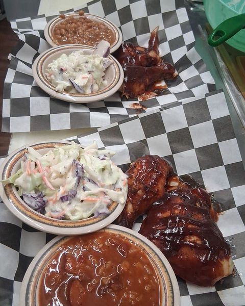 Plates of coleslaw, baked beans and sauced barbecue, and a bowl of red beans, on black-and-white checkered paper