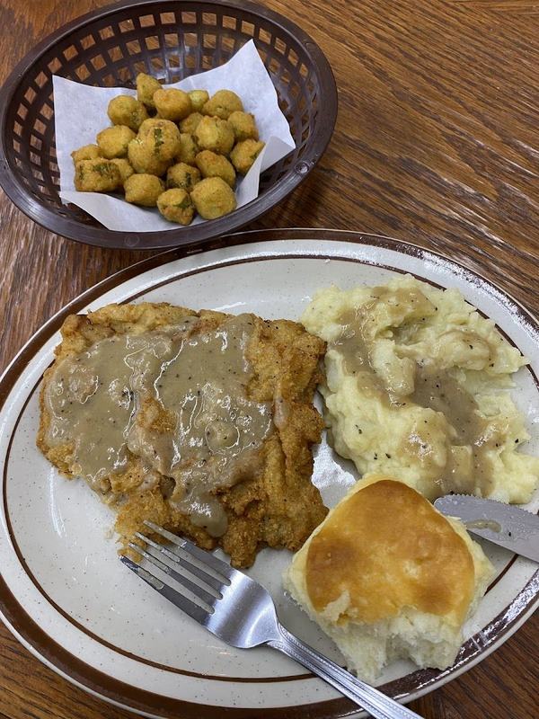 Chicken fried steak covered in gravy beside mashed potatoes and a basket of fried sides