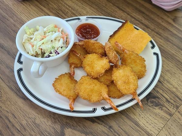 Plate of fried shrimp with a cup of coleslaw and a square of cornbread