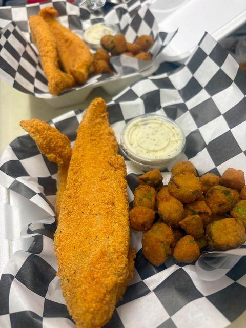 Breaded fried catfish fillets with fried okra and a cup of tartar sauce on checkered paper