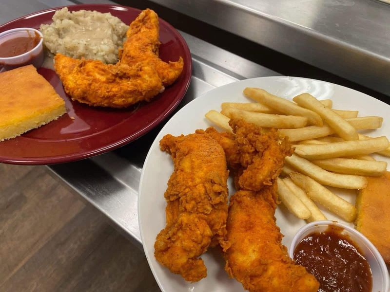 Two plates of fried chicken strips with fries and sauce, and mashed potatoes with gravy and cornbread