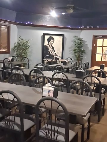 Dining room of Zo's new Indian Creek Mall restaurant: rows of gray tables and black chairs, plants, a framed portrait on the wall and a wood-framed door