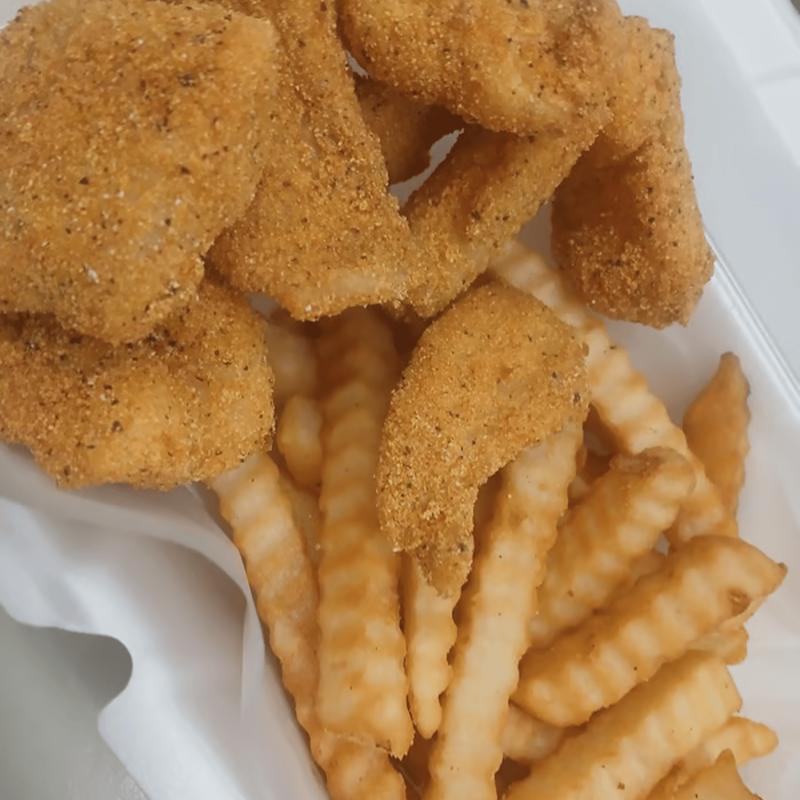 Fried catfish pieces over crinkle-cut fries in a takeout basket